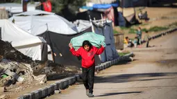 Penelitian tersebut juga menyoroti bahwa anak-anak di Gaza saat ini berada dalam kondisi terlalu lapar, trauma, dan kelelahan untuk dapat belajar atau bermain, yang mengancam masa depan mereka secara permanen. Tampak dalam foto, seorang gadis kecil membawa karung di punggungnya sambil berjalan di sepanjang jalan di kamp pengungsi Nuseirat untuk pengungsi Palestina di utara Deir al-Balah, Jalur Gaza tengah pada 29 Januari 2026. (EYAD BABA/AFP)