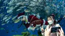 Pengunjung berpose di depan seorang penyelam yang berpakaian seperti Sinterklas saat memberi makan ikan dalam akuarium di Yokohama Hakkeijima Sea Paradise, Yokohama, Jepang, 10 Desember 2021. Walau populasi umat Kristiani hanya 1 persen, perayaan Natal di Jepang tetap meriah. (Philip FONG/AFP)