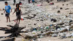 Anak-anak berjalan melewati plastik dan sampah lainnya yang terdampar di Pantai Kedonganan, Kabupaten Badung, Bali, Indonesia, Rabu (12/4/2023). (SONNY TUMBELAKA/AFP)