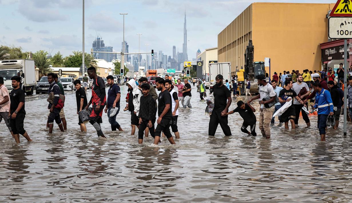 Pusat Meteorologi Nasional UEA telah mengeluarkan peringatan akan adanya hujan di seluruh negeri dari hari Kamis (18/12) sampai Jumat (19/12/2025), termasuk di Dubai dan ibu kota Abu Dhabi. Tampak dalam foto, para pria mengangkat ujung celana mereka untuk menyeberangi genangan air banjir saat melintasi jalan setelah hujan lebat, di Dubai, Uni Emirat Arab (UEA) pada Jumat 19 Desember 2025. (FADEL SENNA/AFP)