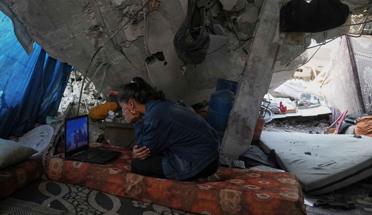 Banyak dari mereka terpaksa tinggal di tenda-tenda darurat, sekolah yang penuh sesak, atau tidur di tempat terbuka di tengah reruntuhan bangunan. Tampak dalam foto, Bisan Taroush menonton film di laptop di bawah atap rumahnya yang sebagian runtuh, menjalani kehidupan sehari-hari di tengah reruntuhan, di Jabaliya, Kota Gaza, Selasa, 11 November 2025. (AP Photo/Jehad Alshrafi)