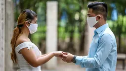 Pasangan berpegangan tangan dalam "pernikahan massal bermasker" di sebuah taman di Kota Makati, Filipina (15/12/2020). Pemerintah Filipina telah memberlakukan kebijakan untuk penggunaan masker di tengah kekhawatiran lonjakan kasus COVID-19 selama musim liburan. (Xinhua/Rouelle Umali)