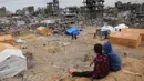 Anak-anak Palestina yang mengungsi duduk di atas gundukan pasir yang menghadap ke tenda-tenda yang didirikan di tengah-tengah bangunan yang hancur di Jabalia, Jalur Gaza utara pada 6 Februari 2025, saat gencatan senjata dalam perang antara Israel dan Hamas. (Bashar TALEB/AFP)
