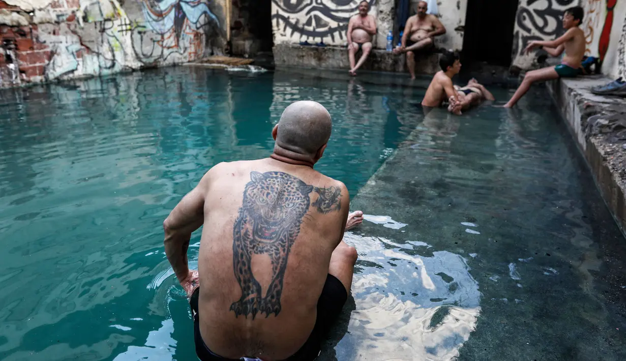 Seorang pria dengan tato macan tutul duduk bersantai di kolam air panas di ujung selatan Dataran Tinggi Golan yang dianeksasi Israel, 1 Maret 2019. Kolam dengan air panas itu berasal dari aliran pipa pengeboran di Lembah Hula. (MENAHEM KAHANA/AFP)