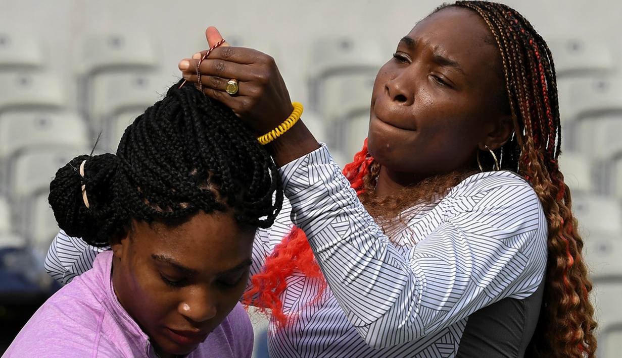 Petenis putri AS, Venus Williams, merapikan rambut adiknya, Serena Williams, saat latihan jelang Olimpiade Rio 2016 di Olympic Tennis Center, Rio de Janeiro, Brasil, (3/8/2016). (AFP/Luis Acosta)