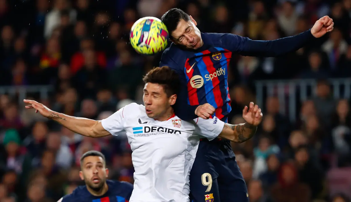 Pemain Barcelona, Robert Lewandowski (kanan) duel udara dengan pemain Sevilla, Gabriel Montiel dalam pertandingan pekan ke-20 La Liga 2022/2023 yang berlangsung di Camp Nou, Senin (6//2/2023). (AP Photo/Joan Monfort)