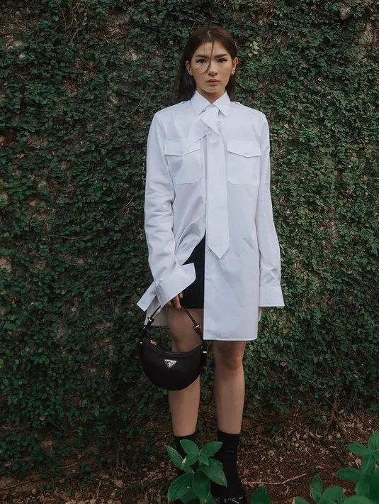 Anastasia Siantar tampil dengan mini skirt warna hitam dipadukan kemeja panjang oversize memiliki aksen kantong depan dan dasi. Dengan membawa handbag hitam senada dengan kaos kaki dan sepatunya. [@anazsiantar]