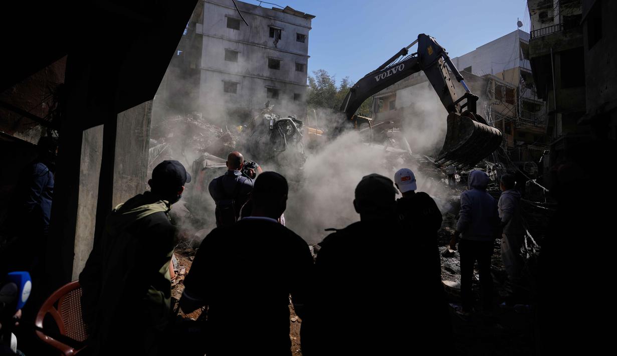 Orang-orang berkumpul saat sebuah ekskavator membersihkan puing-puing di lokasi serangan Israel pada Minggu 5 April 2026 terhadap sebuah bangunan di lingkungan Jnah, Beirut, Lebanon, Senin 6 April 2026. (AP Photo/Hassan Ammar)