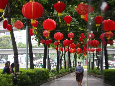 Warga melintas di bawah lampu lampion merah yang terpasang di trotoar kawasan jalan Jenderal Sudirman, Jakarta, Kamis (15/1/2025). (Liputan6.com/Angga Yuniar)