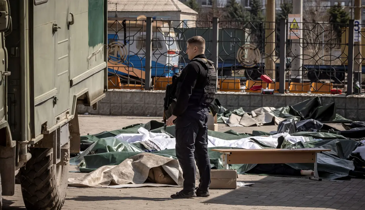 Seorang polisi Ukraina berdiri di dekat mayat yang ditutupi lembaran plastik setelah serangan roket yang digunakan untuk evakuasi sipil di sebuah stasiun kereta api di Kramatorsk, Ukraina timur (8/4/2022). (AFP/Fadel Senna)