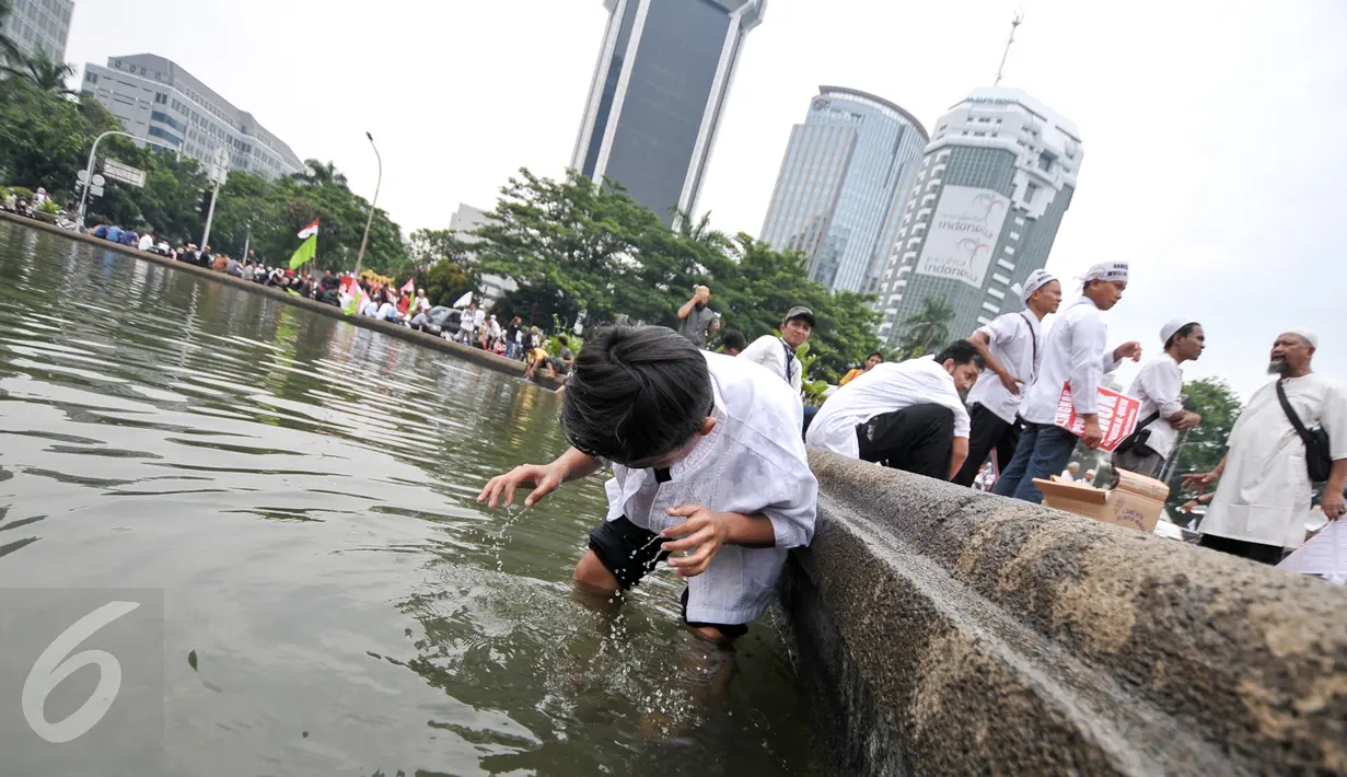 Seorang anak mengambil air wudhu memanfaatkan air di kolam Putaran Patung Kuda, Jakarta, Jumat (4/11). Sebagian massa demonstan gelar salat Jumat di area Bundaran Patung Kuda. (Liputan6.com/Yoppy Renato)
