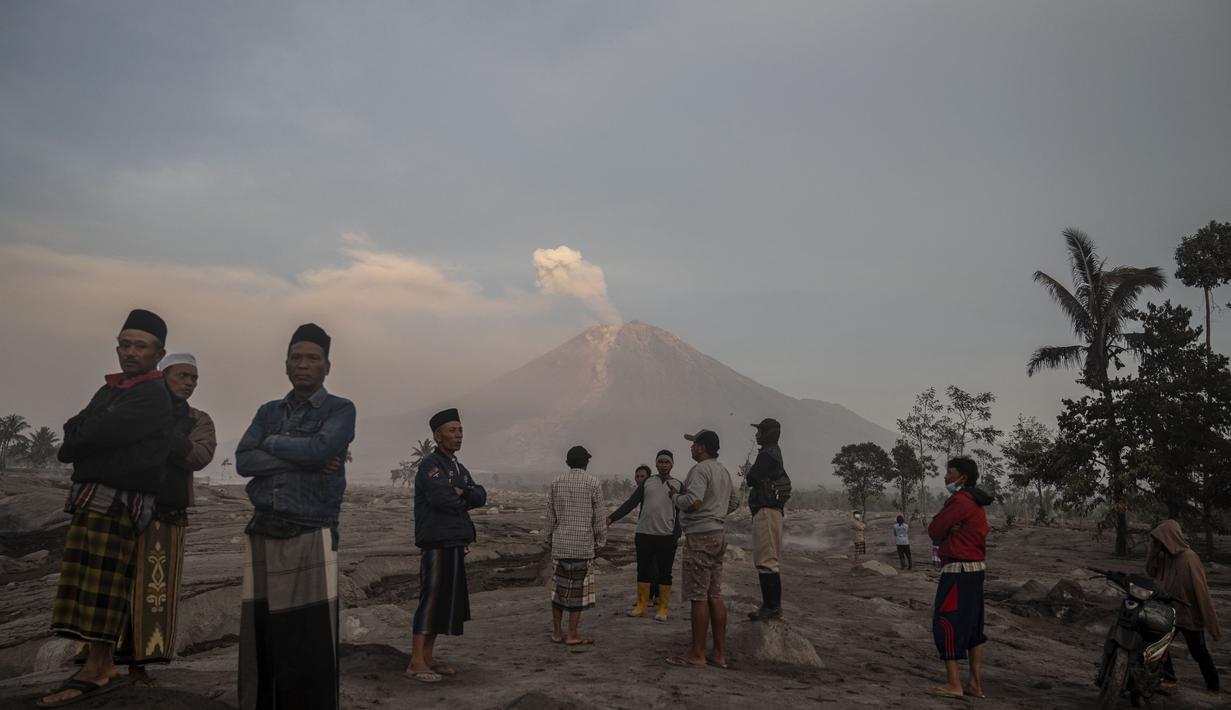 Orang-orang berdiri di depan Gunung Semeru menyusul letusan gunung berapi di desa Kajar Kuning di Lumajang (5/12/2022). Gunung Semeru meletus pada tanggal 4 Desember memuntahkan awan abu panas setinggi satu mil dan sungai lava di sisinya sambil memicu evakuasi hampir 2.000 orang tepat satu tahun setelah letusan besar terakhirnya menewaskan puluhan orang. (AFP/Juni Kriswanto)