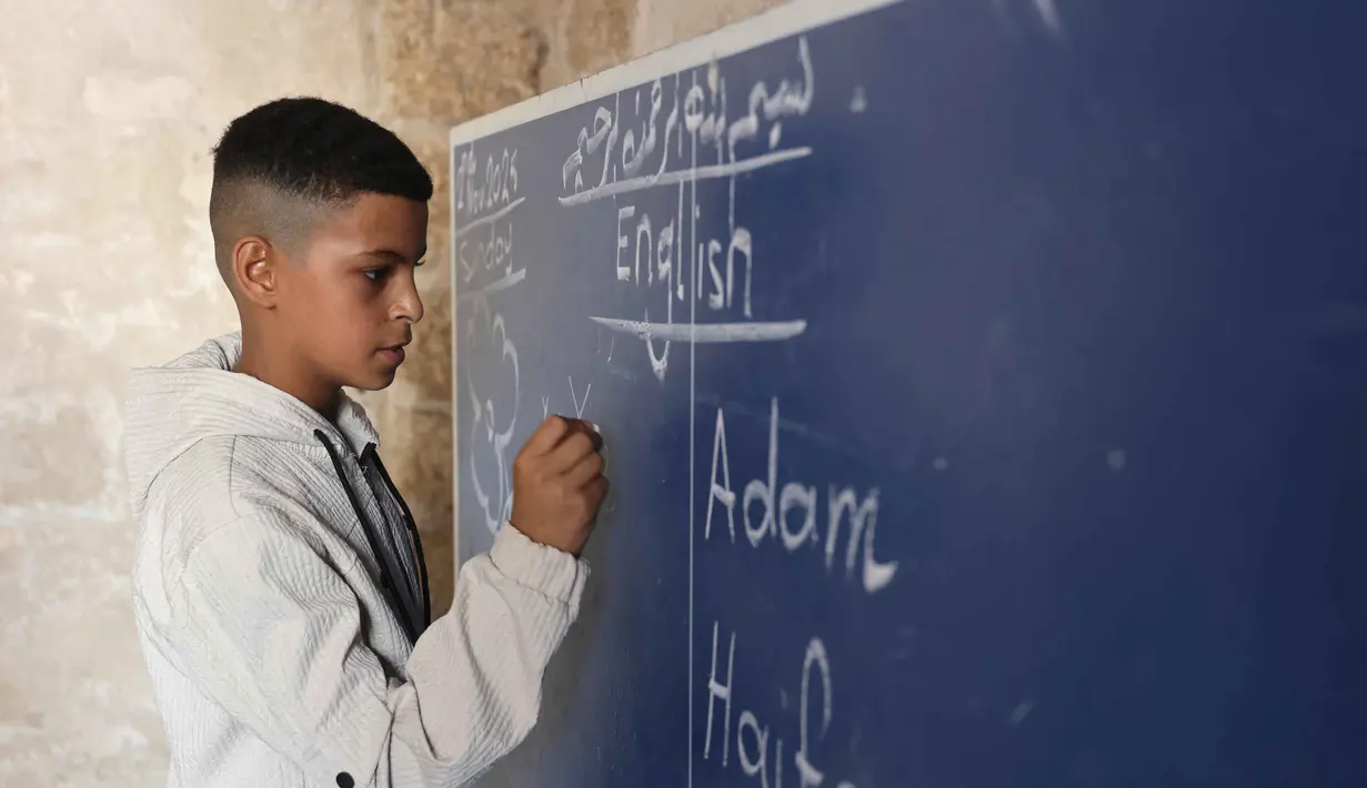 Seorang anak laki-laki Palestina berdiri di depan papan tulis saat pelajaran Bahasa Inggris di sekolah bersejarah "Al-Kamaliya al-Othmanya" di Kota Tua Gaza yang menjadi bagian dari inisiatif sukarelawan yang diorganisir oleh para guru pengungsi, di Kota Gaza pada 2 November 2025. Seiring berlakunya gencatan senjata, berbagai upaya mulai dilakukan secara bertahap untuk melanjutkan proses pembelajaran. (Omar AL-QATTAA/AFP)