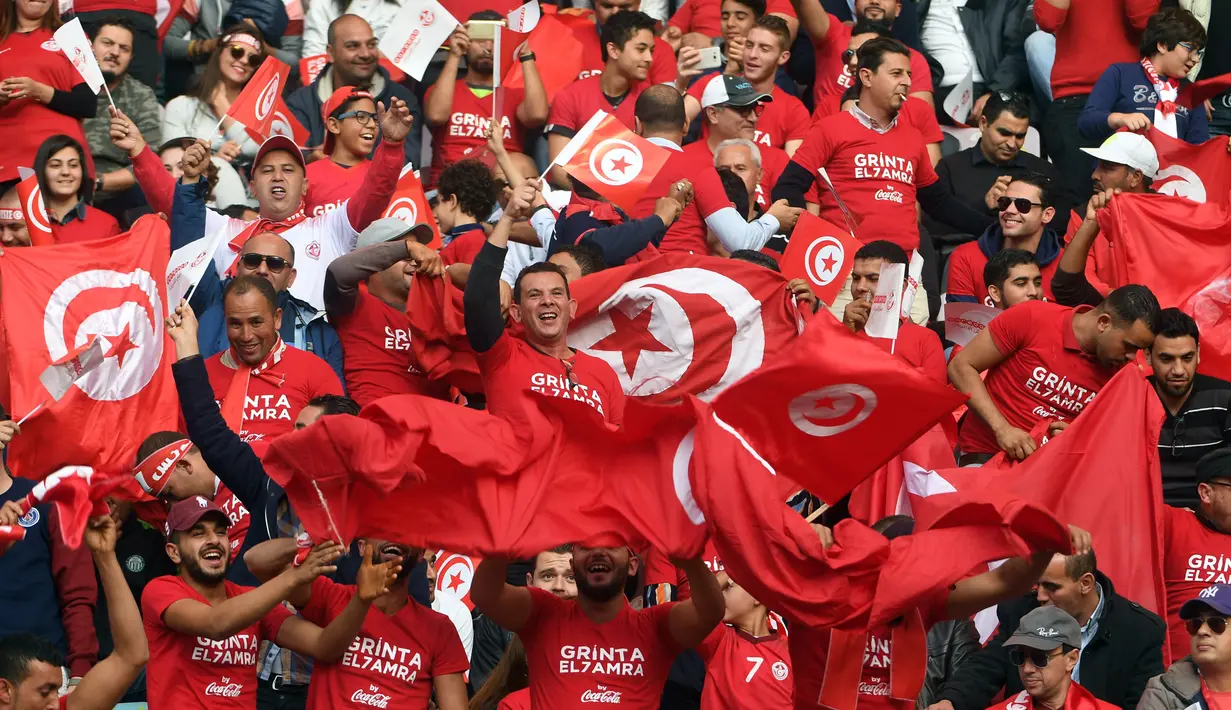 Pendukung Timnas Tunisia mengibarkan bendera dan meneriakan yel-yel saat menyaksikan pertandingan antara Tunisia melawan Libya di kualifikasi Piala Dunia 2018 di Stadion Olimpiade Rades, Tunisia (11/11). (AFP Photo/Fethi Belaid)