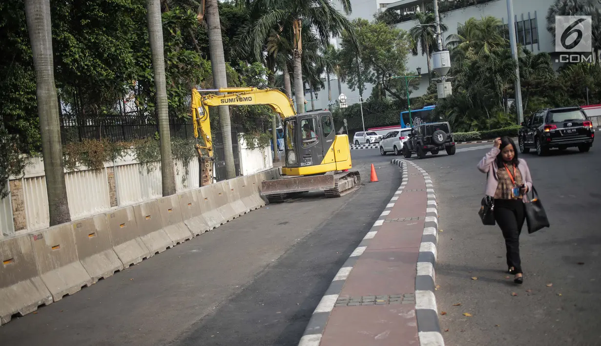Pejalan kaki melintas saat pekerja dibantu alat berat merevitalisasi trotoar di kawasan Bundaran HI, Jakarta Pusat, Senin (15/7/2019). Penantaan ini dilakukan untuk mempercantik trotoar dan memberikan rasa nyaman bagi pejalan kaki. (Liputan6.com/Faizal Fanani)