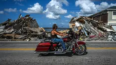 Seorang pengendara sepeda motor melewati puing-puing yang menumpuk dari rumah yang hancur setelah melewati Badai Ian di Pulau Matlacha di Lee County, Florida pada 7 November 2022. Pantai timur Florida berada di bawah pengawasan badai saat negara bagian itu bergulat dengan kehancuran Badai Ian. (AFP/ Giorgio Viera)