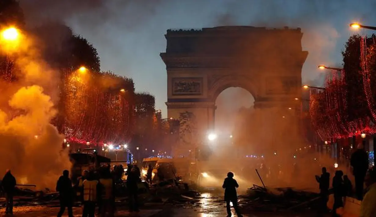 Asap membumbung dekat Arc de Triomphe saat kerusuhan menentang kenaikan harga bahan bakar di Paris, Prancis, Sabtu (24/11). Polisi memasang penghalang logam di sekitar Champs-Élysées untuk menghentikan pergerakan demonstran. (AP Photo/Christophe Ena)