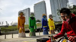 Pesepeda melintasi ondel-ondel yang dipasang di Taman Ismail Marzuki (TIM), Jakarta, Selasa (22/6/2021). Sebanyak 10 ondel-ondel raksasa setinggi 4,94 meter akan dipamerkan di TIM saat peringatan HUT ke-494 DKI Jakarta yang berlangsung dari 22 hingga 30 Juni 2021. (Liputan6.com/Faizal Fanani)