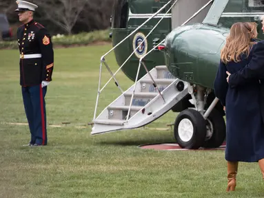 Presiden AS Donald Trump terlihat memegang ibu negara, Melania Trump yang hampir terjatuh saat berjalan menuju helikopter kepresidenan di halaman berumput Gedung Putih, Senin (19/3). Trump dan Melania hendak bertolak ke New Hempshire. (JIM WATSON/AFP)