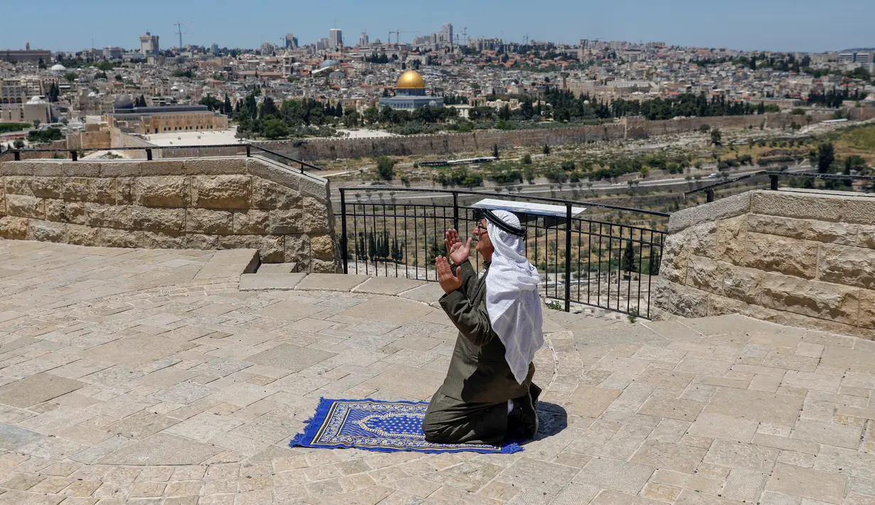 Seorang pria Palestina melaksanakan salat Jumat saat bulan Ramadan di depan Bukit Zaitun dengan latar belakang kota tua Yerusalem dan Masjid Al-Aqsa yang ditutup, Jumat (8/5/2020). Masjid Al-Aqsa telah ditutup sejak bulan lalu untuk mencegah penyebaran Covid-19. (Photo by AHMAD GHARABLI / AFP)