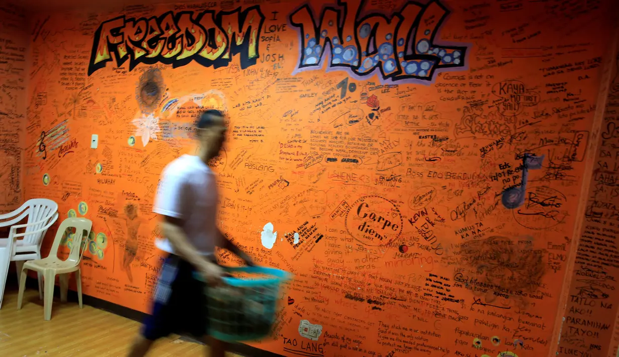 Pasien rehabilitasi membawa pakaian saat melintas di depan tembok bertuliskan "Freedom Wall" di Pusat Pemulihan Kristen di Antipolo, Filipina (12/9). (REUTERS/Romeo Ranoco)