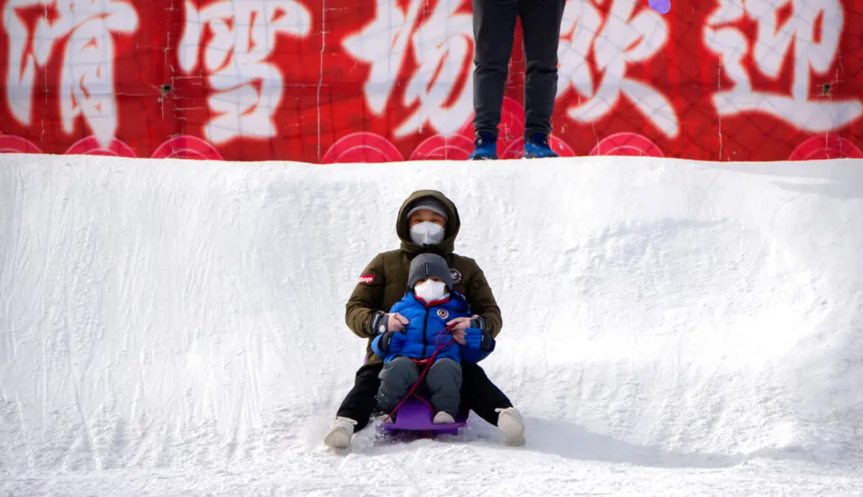 Seorang wanita dan anak-anak yang mengenakan masker meluncur menuruni bukit tertutup salju menggunakan kereta luncur di taman umum saat pekan liburan Tahun Baru Imlek di Beijing, China, Kamis (26/1/2023). (AP Photo/Mark Schiefelbein)