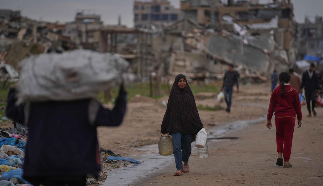 Kondisi infrastruktur sanitasi dan air bersih yang sudah rusak akibat perang, semakin tertekan oleh hujan deras, meningkatkan risiko penyebaran penyakit akibat genangan air limbah dan sampah. Tampak dalam foto, seorang wanita Palestina membawa wadah berisi air di Nuseirat, Jalur Gaza tengah, Jumat, 2 Januari 2026. (AP Photo/Abdel Kareem Hana)