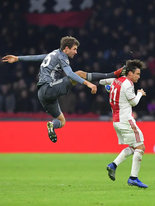 Gelandang Bayern Munchen Thomas Mueller (kiri) menendang kepala bek Ajax Amsterdam Nicolas Tagliafico dalam laga Grup E Liga Champions di Amsterdam, Belanda, Rabu (12/12). Mueller disebut tak sengaja saat insiden itu terjadi. (EMMANUEL DUNAND/AFP)