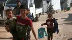 Anak-anak Suriah yang terlantar membawa pakaian yang disumbangkan oleh organisasi amal lokal berjalan kembali ke tenda mereka di sebuah kamp di pinggiran kota Dana yang dikuasai pemberontak, di sebelah timur perbatasan Turki-Suriah di provinsi barat laut Idlib (30/4/2022). (AFP/Aaref Watad)