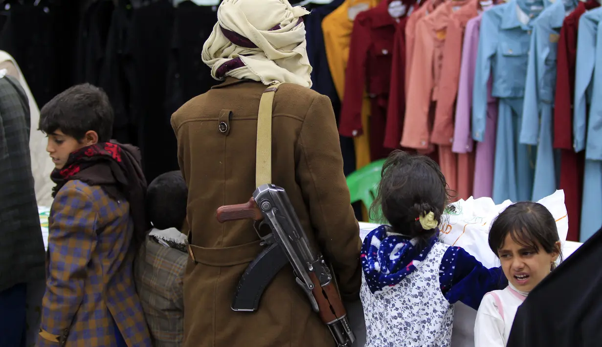 Seorang pria yang membawa senapan AK47 menemani anak-anak di ruang pamer membagikan pakaian kepada pemuda yang kehilangan orang tua dalam konflik, sebagai bagian dari kegiatan amal selama bulan suci Ramadhan, di ibu kota Sanaa (8/4/2022). (AFP/Mohammed Huwais)