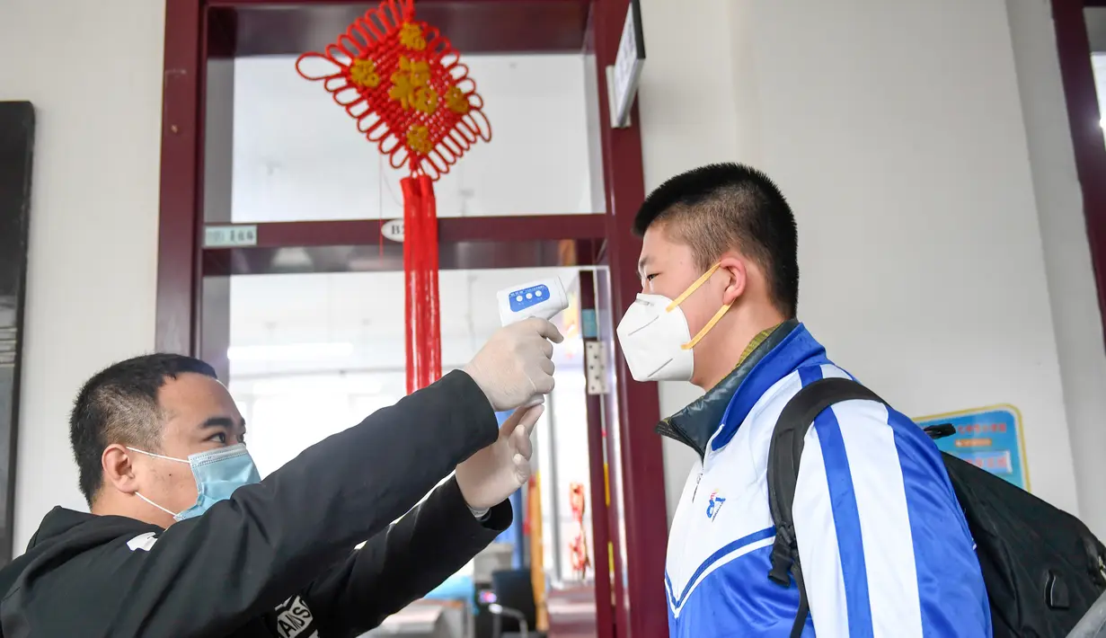 Seorang staf memeriksa suhu tubuh seorang murid di Sekolah Menengah Pertama No. 87 di Changchun, Provinsi Jilin, China timur laut, (20/4/2020). Lebih dari 56.000 pelajar tahun akhir sekolah menengah pertama di Changchun kembali masuk sekolah pada Senin (20/4). (Xinhua/Yan Linyun)