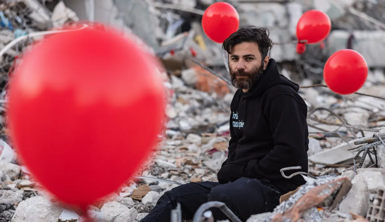 Ogun Sever Okur, pria Turki berusia 38 tahun berpose di antara balon yang tergantung di puing-puing bangunan yang runtuh di Antakya, Turki selatan pada 21 Februari 2023, menyusul gempa berkekuatan 6,4 yang melanda pada 20 Februari, dua minggu setelah gempa berkekuatan 7,8 -gempa berkekuatan melanda dekat Gaziantep dan telah menewaskan lebih dari 44.000 orang.