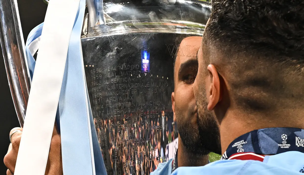 Gelandang Manchester City, Riyad Mahrez mencium trofi Liga Champions dalam perayaan kemenangan atas Inter Milan pada laga Final Liga Champions 2022/2023 di Ataturk Olympic Stadium, Istanbul, (10/6/2023). Gelar ini juga menjadi yang pertama baginya. (AFP/Paul Ellis)