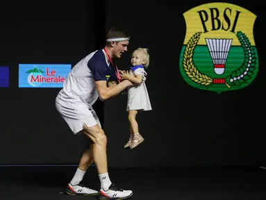 Pebulu tangkis tunggal putra Denmark, Viktor Axelsen, menggendong anaknya usai berhasil menjadi pemenang di nomor tunggal putra Indonesia Open 2022 usai mengalahkan pebulu tangkis tunggal putra China, Zhao Jun Peng pada babak di Istora Senayan, Jakarta, Minggu (19/06/2022). (Bola.com/Bagaskara Lazuardi)