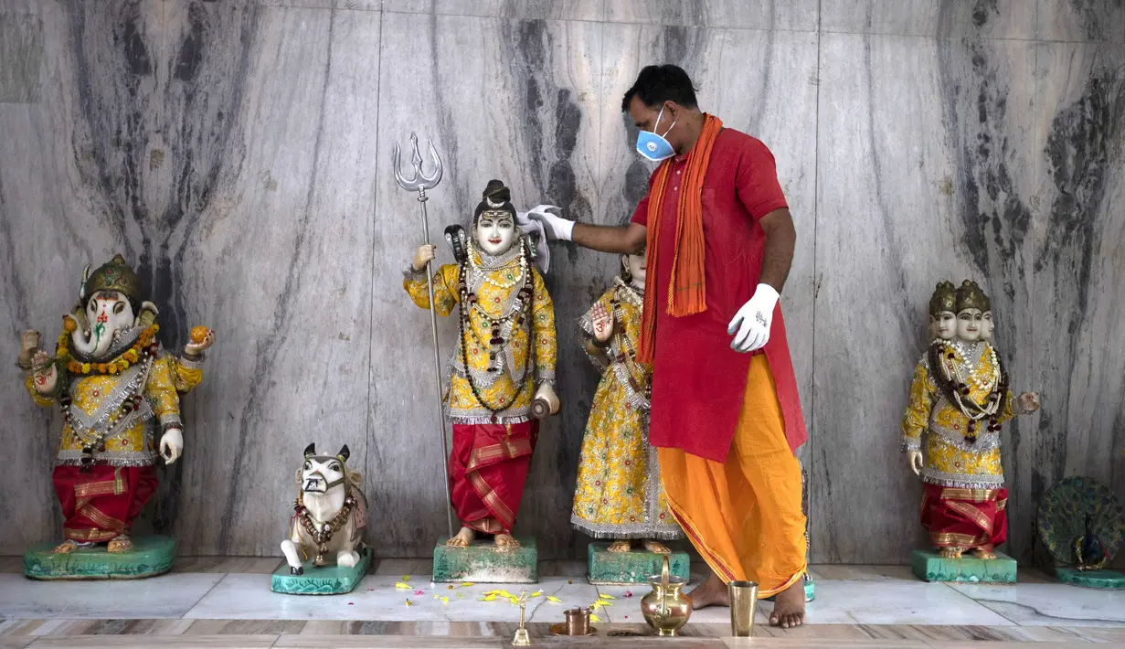 Seorang pendeta membersihkan patung Dewa Siwa dan dewa-dewa Hindu lainnya di sebuah kuil di Prayagraj, India, Senin (8/6/2020). India kembali membuka tempat ibadah, pusat perbelanjaan, dan restoran setelah tiga bulan lockdown karena pandemi virus corona COVID-19. (AP Photo/Rajesh Kumar Singh)