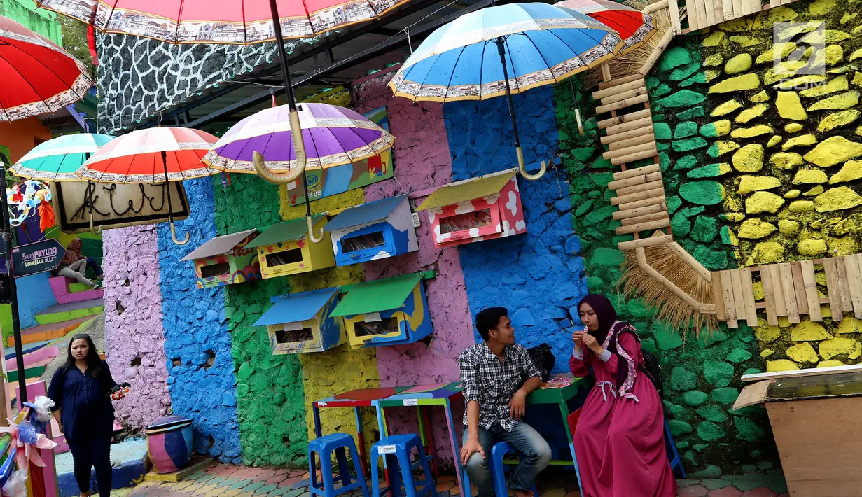 Wisatawan sedang melintas dan duduk berbincang di kampung warna-warni, Kelurahan Kesatrian, Kota Malang, Minggu (5/11). Lukisan di kampung tersebut melibatkan komunitas mural dan seniman. (Liputan6.com/Fery Pradolo)
