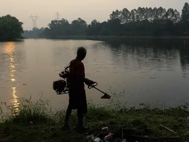 Warga memotong rumput di situ Sawangan di kawasan Sawangan, Depok, Jawa Barat, Kamis (27/7/2023). (Liputan6.com/Herman Zakharia)