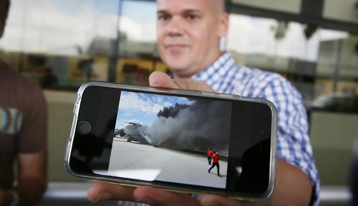 Seorang penumpang menunjukkan gambar dari pesawat milik maskapai Dynamic International Airways yang terbakar saat akan lepas landas di Bandara Fort Lauderdale, Florida, Kamis (29/10). 15 orang terluka akibat kejadian tersebut (Joe Raedle/Getty Images/AFP)