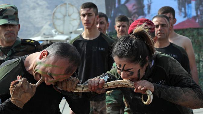 Pasukan perempuan Peshmerga bersama seorang pria menggigit ular saat berlatihan dalam upacara kelulusan di Kota Soran, Irak, Rabu (12/2/2020). Latihan militer pasukan bersenjata Kurdi tersebut dilakukan sekitar 100 kilometer timur laut ibu kota otonomi wilayah Kurdi di Irak, Arbil. (SAFIN HAMED/AFP)