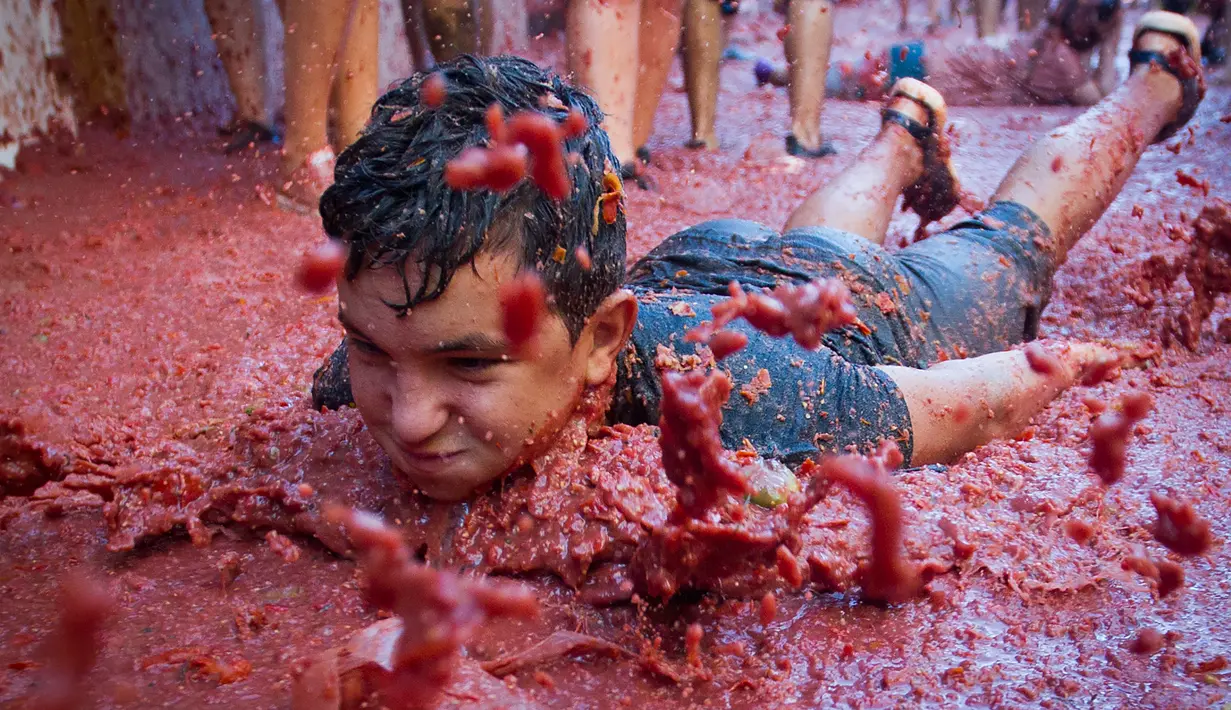 Peserta bersuka ria dengan tomat yang hancur saat festival tahunan "Tomatina" di Bunol, salah satu kota di timur Spanyol, Rabu (29/8/2019). Digelar sejak 1945, perang tomat ini menjadi daya tarik utama bagi wisatawan mancanegara seperti dari Inggris, Jepang, dan AS. (JAIME REINA / AFP)