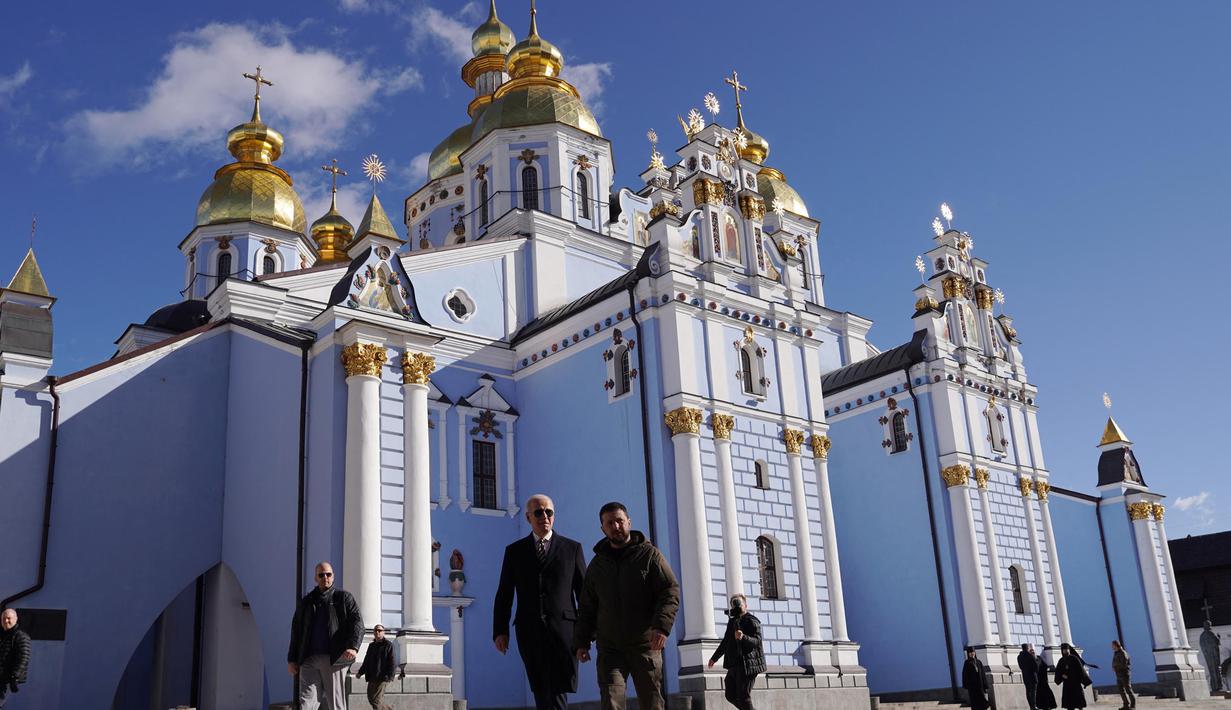 Presiden AS Joe Biden (kiri) berjalan di samping Presiden Ukraina Volodymyr Zelensky di depan Katedral Kubah Emas Santo Mikhael ketika ia tiba untuk kunjungan di Kyiv, Ukraina pada 20 Februari 2023. Presiden AS Joe Biden melakukan kunjungan mendadak ke Kyiv menjelang peringatan satu tahun invasi Rusia ke Ukraina. Biden bertemu dengan Presiden Ukraina Volodymyr Zelensky di ibu kota Ukraina dalam kunjungan pertamanya ke negara itu sejak dimulainya konflik. (Dimitar DILKOFF/AFP)