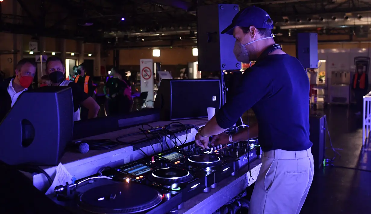Seorang DJ tampil saat orang-orang tiba untuk menerima vaksinasi virus corona COVID-19 di pusat vaksinasi Arena Treptow, Berlin, Jerman, Senin (9/8/2021). Vaksinasi dengan diiringi musik DJ tersebut berlangsung pada malam yang panjang di tengah pandemi COVID-19. (John MACDOUGALL/POOL/AFP)