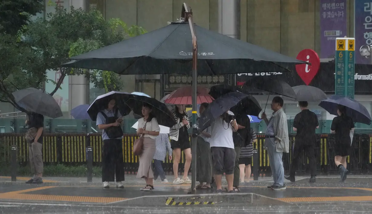 Orang-orang terlihat berdiri di bawah kanopi peneduh saat hujan deras mengguyur di Seoul, Korea Selatan, Rabu, 17 Juli 2024. (AP Photo/Ahn Young-joon)