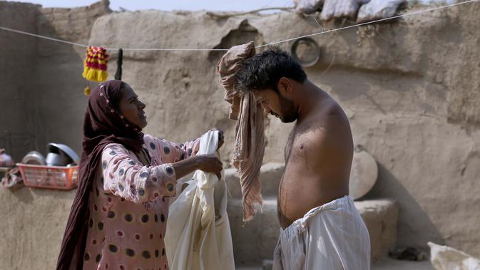 Rizia Bibi membantu putranya Mohammad Ikram, yang bermain snooker dengan dagu, mengenakan kemeja panjang di rumahnya di sebuah desa dekat kota Samundri, Pakistan, Minggu (25/10/2020). (AP Photo/Anjum Naveed)