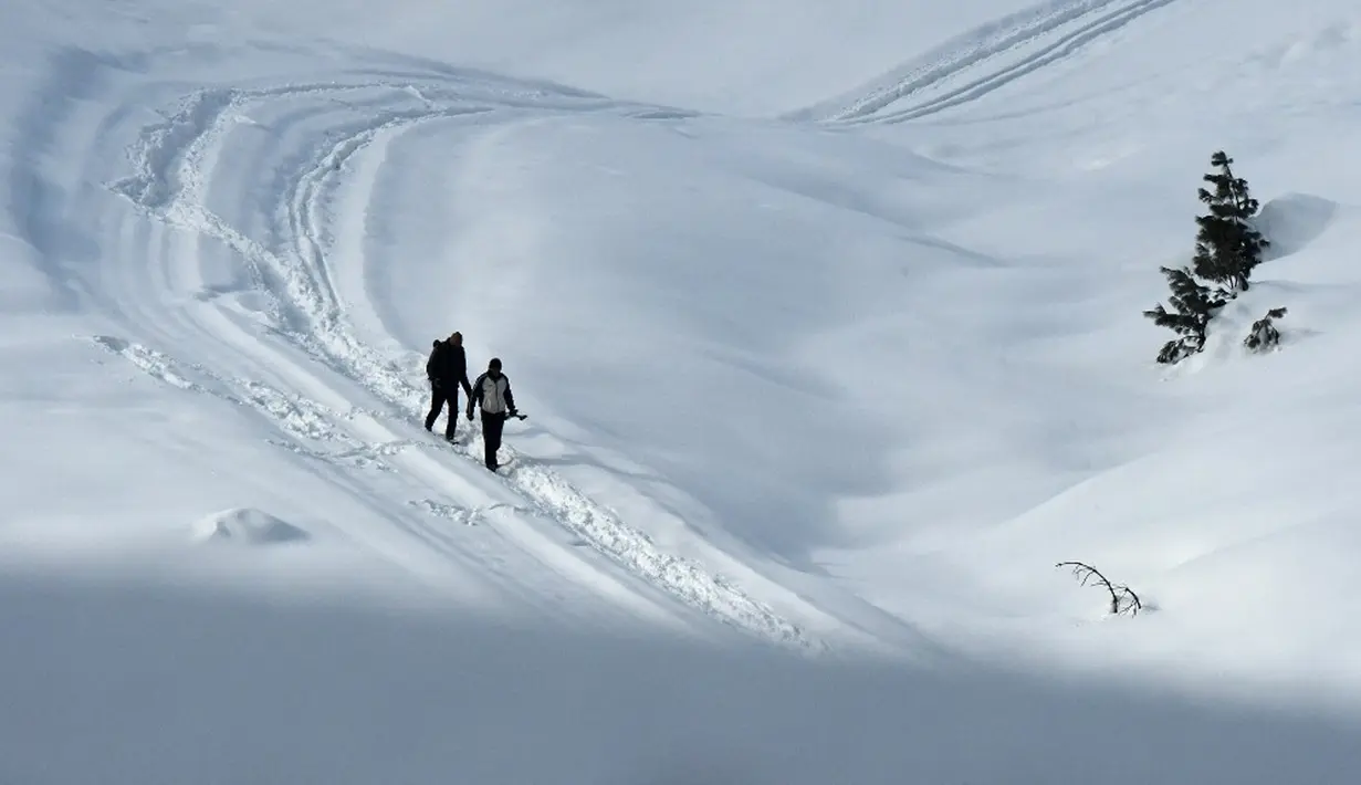 Orang-orang berjalan melewati salju di resor ski di Gulmarg, sekitar 55 km utara Srinagar, Jammu dan Kashmir, India, 25 Januari 2021. Ketika musim dingin tiba, perjalanan dari Srinagar ke Gulmarg akan menyuguhkan lansekap gunung-gunung berselimut salju yang kokoh dan beku. (Tauseef MUSTAFA/AFP)