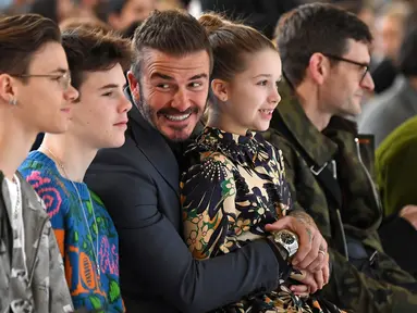 David Beckham bersama anak-anaknya Romeo Beckham, Cruz Beckham dan Harper saat menghadiri peragaan busana Musim Gugur/Musim Dingin 2020 Victoria Beckham dalam acara London Fashion Week di London, (16/2/2020). Beckham tampil dengan setelan jas hitam. (AFP/Daniel Leal-Olivas)