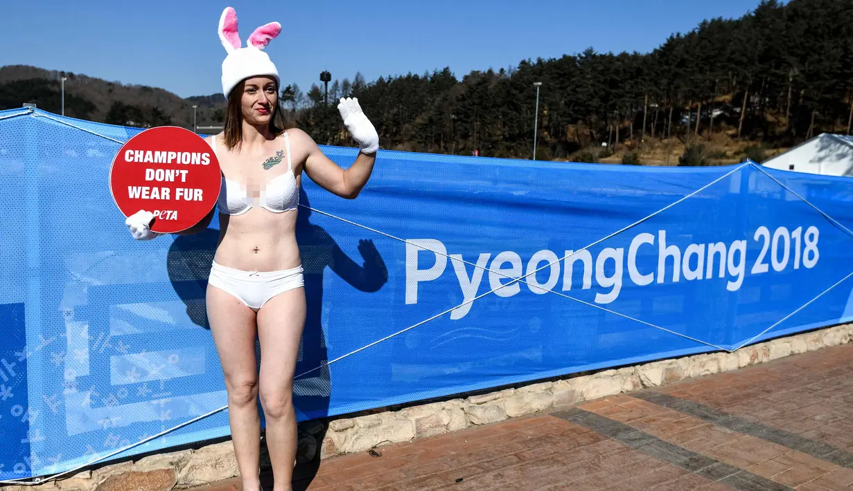 Seorang aktivis wanita dari PETA berunjuk rasa di samping spanduk Olimpiade Pyeongchang 2018 di Pyeongchang, Korea Selatan (6/2). Aktivis ini nekat tampil berbikini saat unjak rasa berlangsung. (AFP Photo/Dimitar Dilkoff)