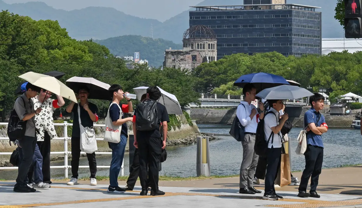 Otoritas setempat meminta warga untuk tetap berada di dalam ruangan, menggunakan pendingin, menjaga hidrasi, serta menghindari aktivitas luar ruang di jam-jam puncak panas. Tampak dalam foto, sekelompok wisatawan menggunakan payung di tengah teriknya musim panas sambil menunggu cahaya berganti, dengan Kubah Bom Atom di latar belakang pusat kota Hiroshima pada 5 Agustus 2025. (Richard A. Brooks/AFP)