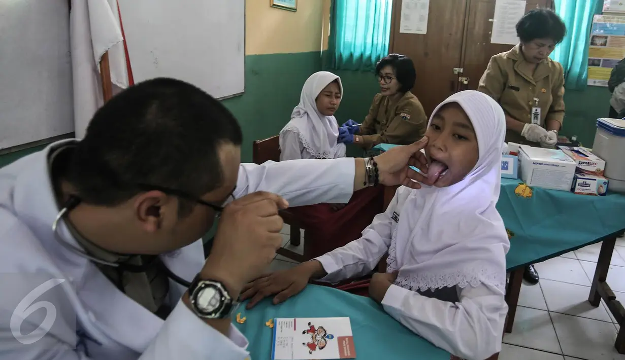 Dokter memeriksa seorang anak saat mengikuti Bulan Imunisasi Anak sekolah (BIAS) di SDN 11 Pagi, Lubang Buaya, Jakarta, Selasa (4/10). Kegiatan ini untuk mewujudkan Indonesia bebas dari kanker serviks. (Liputan6.com/Faizal Fanani)