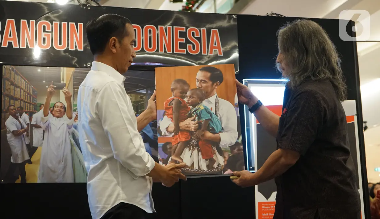 Presiden Joko Widodo atau Jokowi menerima foto dari kurator Oscar Motuloh dalam pameran foto 'Membangun Indonesia'  di Jakarta, Selasa (12/11/2019). Pameran foto itu menampilkan sejumlah capaian kinerja pemerintahan Presiden Joko-Widodo dan Wakil Presiden Jusuf Kalla. (Liputan6.com/Angga Yuniar)
